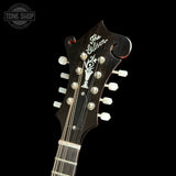 Close-up of the headstock of a Gibson electric guitar against a black background, showing the Gibson logo, tuning pegs, and strings. A Tone Shop watermark is visible in the top left corner.