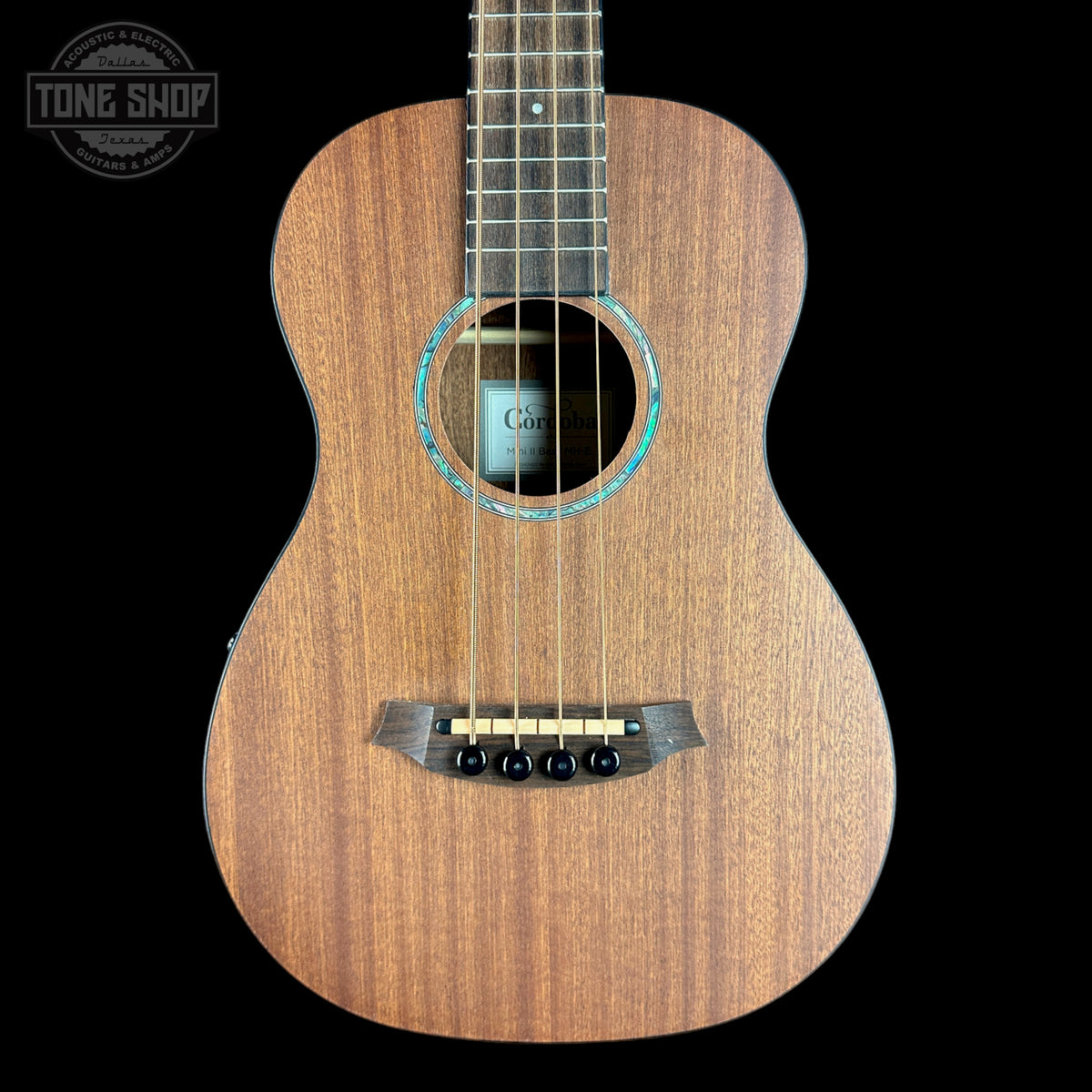 Small wooden guitar with a black pickguard on a black background, featuring the Tone Shop logo.