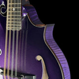 Close-up of a purple electric guitar body with a fluted wood finish, gold-toned binding, and part of the fretboard visible against a black background.
