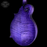 Close-up of the back of a mandolin with a vibrant purple iridescent finish and prominent figured wood grain, set against a solid black background. A Tone Shop watermark is visible in the top-left corner.