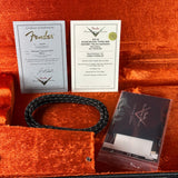 Fender certificate of authenticity, guitar cable, and branded case on an orange surface