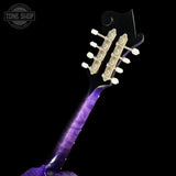 Close-up of the headstock and upper neck of an electric guitar against a black background, showing a glossy purple flamed maple finish and gold-toned tuning pegs. A Tone Shop watermark is visible in the top left corner.