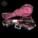 A vintage black mandolin in an open black hard case with a bright pink velvet interior, photographed against a solid black background. A Tone Shop watermark is visible in the top left corner.