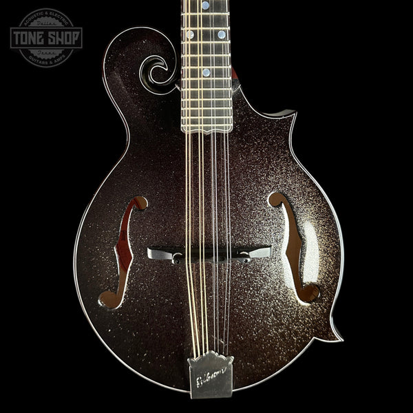 A close-up studio shot of a Gibson mandolin against a solid black background, featuring a dark brown glitter finish with gold sparkle, silver hardware, and a white Gibson logo on the bridge plate.