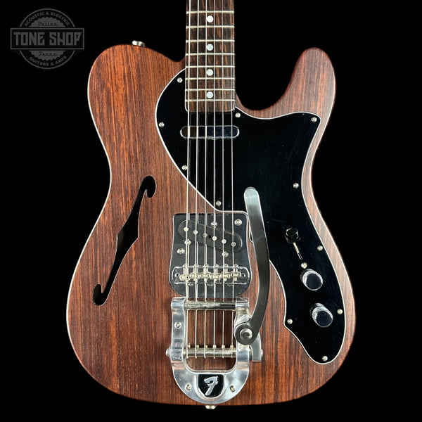Wooden electric guitar with a black pickguard on a black background, featuring the Tone Shop logo.