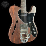Wooden electric guitar with a black pickguard on a black background, featuring 'Tone Shop' branding.