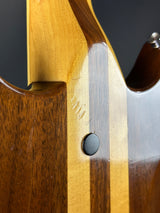 Close-up of a wooden guitar neck with a metal truss rod and black button.