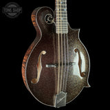 A close-up studio shot of a mandolin against a solid black background. The mandolin features a dark brown glitter finish on the body, a natural wood grain side edge, and a silver metal neck and bridge.