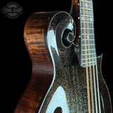 Close-up of a custom electric guitar body featuring a dark glitter finish with gold swirl patterns and a natural brown wood grain on the side, with part of the fretboard and strings visible against a black background.