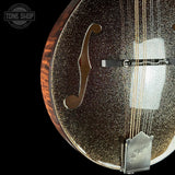 Close-up of a mandolin with a glittering gold-flecked finish and a dark wood edge, shown against a black background with a Tone Shop watermark.