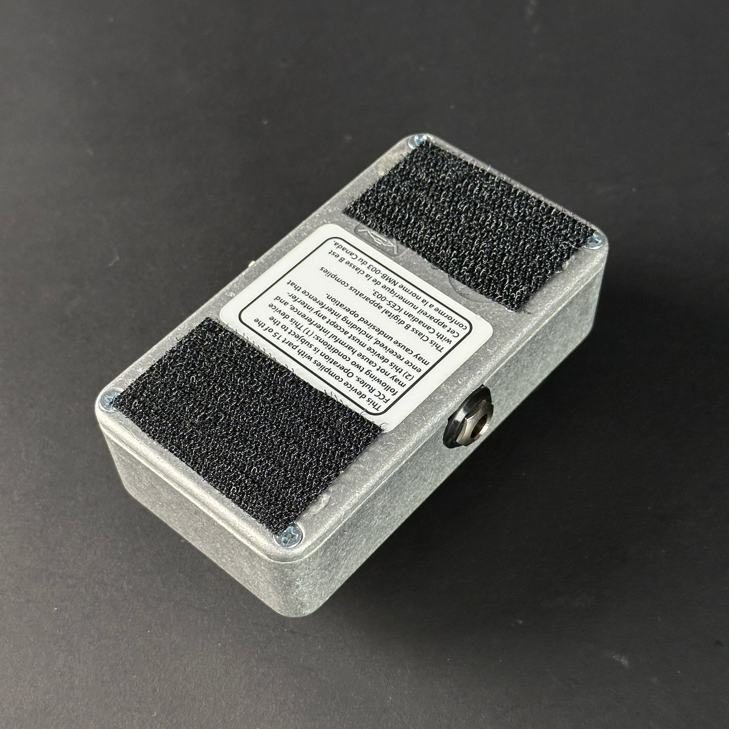 Small rectangular device with black foam pads on a dark background