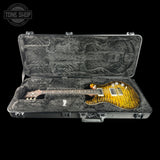 An electric guitar with a yellow-orange flame maple body and dark neck, displayed inside an open black hard case with gray foam lining against a black background. A Tone Shop logo watermark is visible in the top left corner.