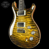 A close-up of an electric guitar body featuring a vibrant golden-yellow flamed maple wood finish with dark brown wavy grain patterns. The guitar has chrome hardware, white pickguard, and a black headstock partially visible at the top edge.