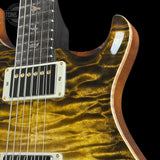 Close-up of an electric guitar body showing a glossy flamed maple top in a metallic gold finish, a white humbucker pickup, and part of the dark fretboard against a black background.