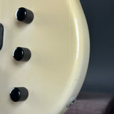 Close-up of a cream-colored guitar with black knobs on a dark background