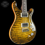 A close-up of an electric guitar body featuring a vibrant golden-yellow flamed maple wood finish with natural wavy grain patterns. The guitar has chrome hardware, dual humbucker pickups, and a dark fretboard, shown against a solid black background with a Tone Shop watermark in the top-left corner.