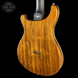 The back of an electric guitar with a glossy, warm honey-amber wood finish, shown against a solid black background. A Tone Shop watermark is visible in the top-left corner.