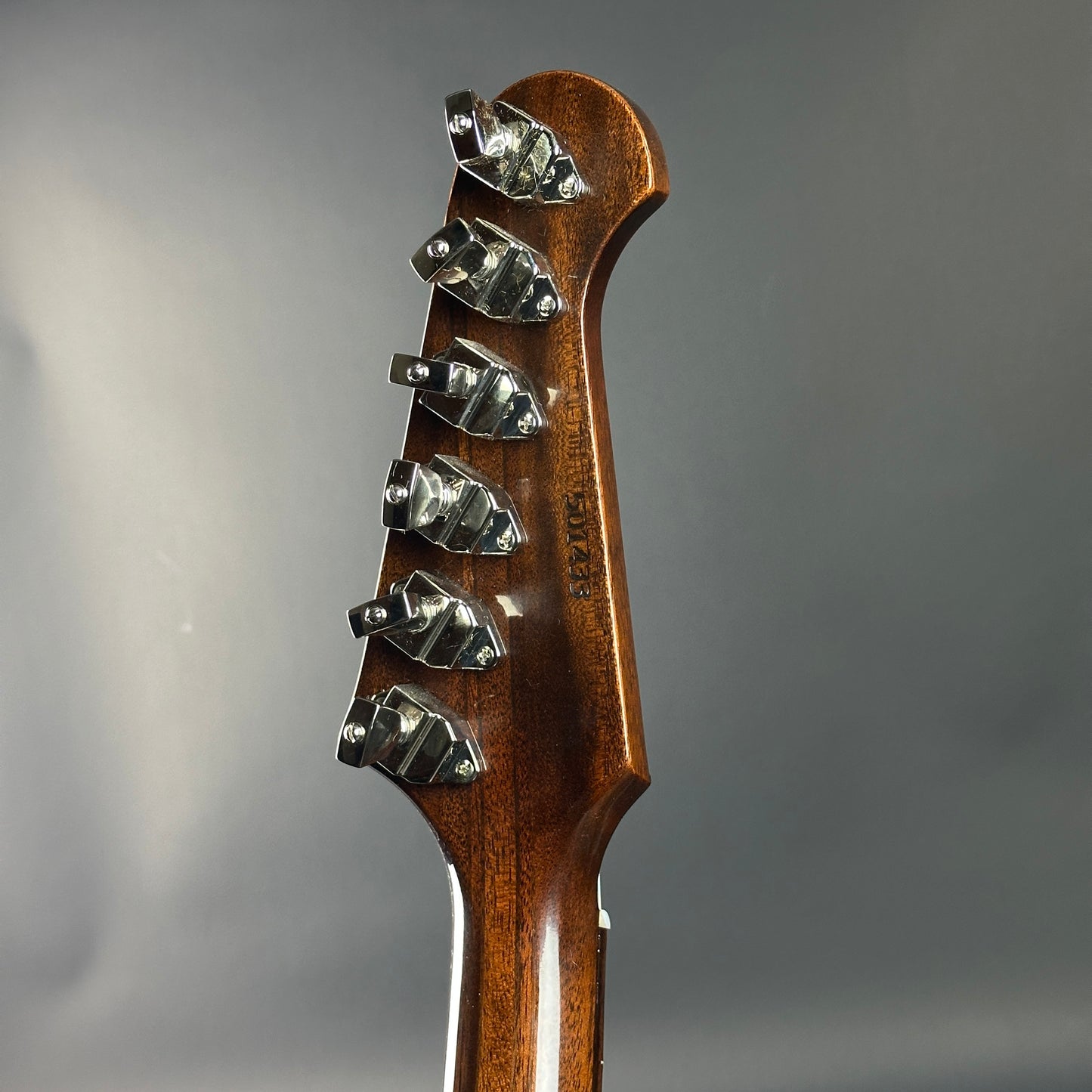 Close-up of a guitar headstock with tuning pegs on a gray background