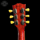 Close-up of the headstock of a guitar with a glossy reddish-brown wood finish, six yellow tuning pegs, and black tuning machines, shown against a black background with a Tone Shop watermark in the top left.