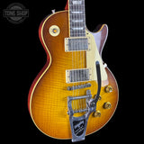 A Gibson Les Paul Custom electric guitar with a sunburst finish, featuring a flame maple top, gold hardware, and a silver Biggestopper tailpiece, shown against a solid black background.