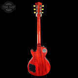 A red wood finish electric guitar shown from the back, featuring a glossy cherry-red wood body, black pickguard, and gold tuning pegs, set against a solid black background with a Tone Shop watermark in the top left.