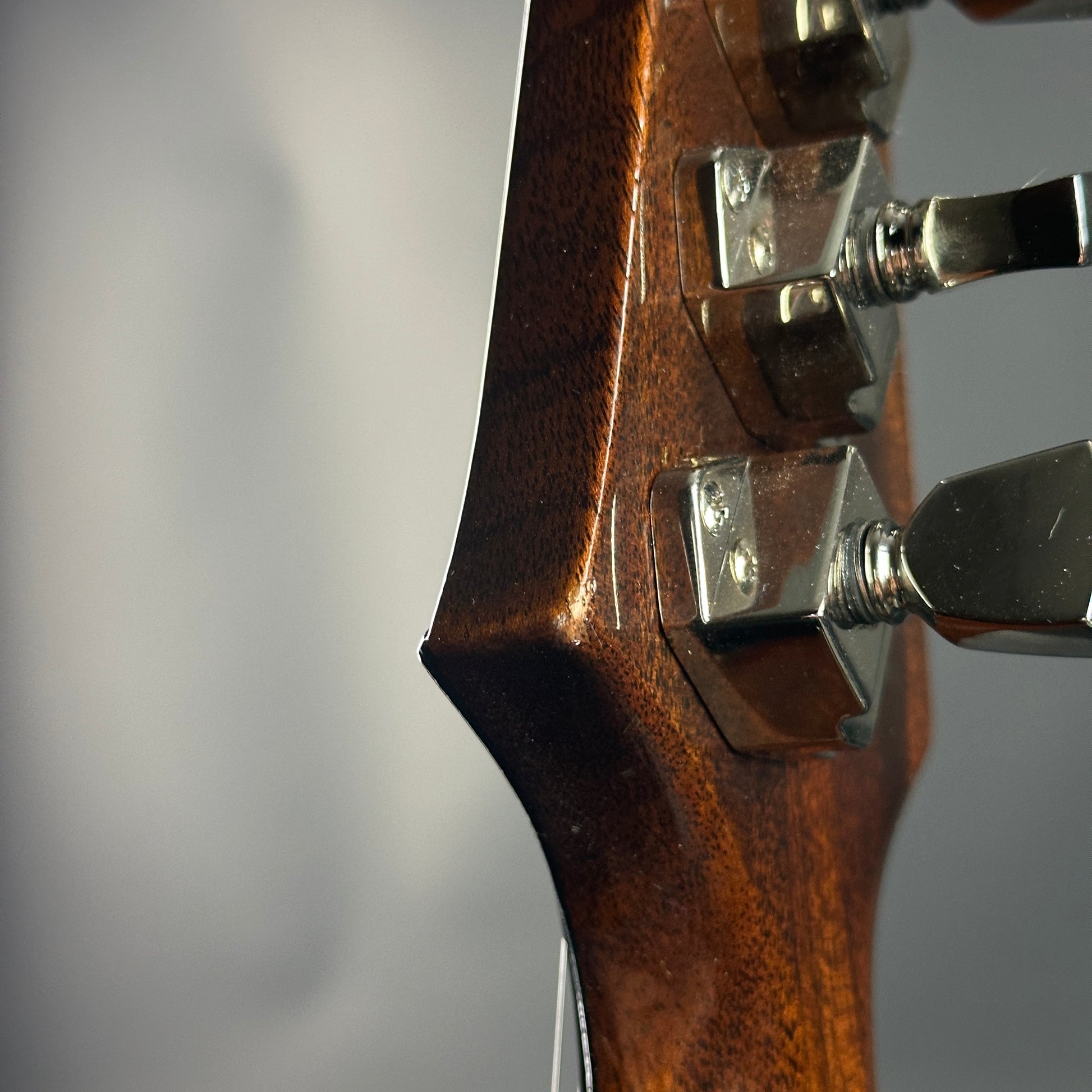 Close-up of a guitar headstock with tuning pegs on a blurred gray background