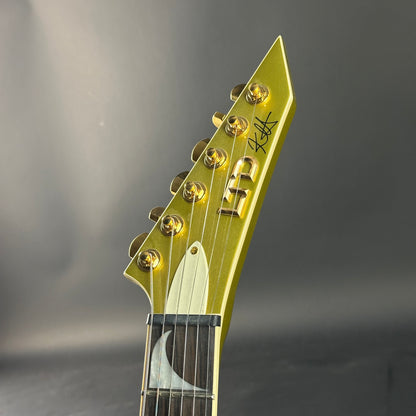 Gold guitar headstock with brand logo on a gray background