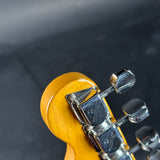 Close-up of a guitar headstock showing the glossy yellow-orange maple top, chrome tuning pegs, and dark background.
