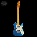 A blue electric guitar with a white pickguard and maple neck, shown against a solid black background. A Tone Shop watermark is visible in the top-left corner.