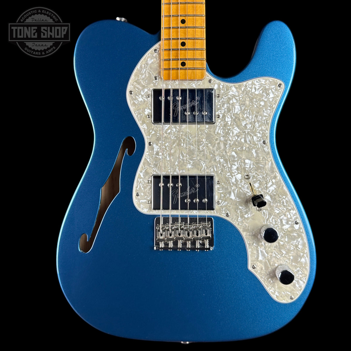 A blue electric guitar with a white pearlescent pickguard and maple neck, shown against a black background with a Tone Shop watermark in the top left corner.