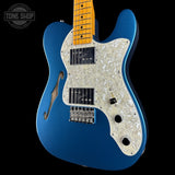 A blue electric guitar with a white pearloid pickguard and maple neck, shown against a black background with a Tone Shop watermark in the top left corner.
