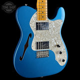 A blue electric guitar with a white mother-of-pearl pickguard and maple neck, shown against a solid black background with a Tone Shop watermark in the top left corner.