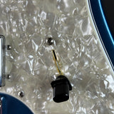 Close-up of a guitar body showing a black volume control jack on a pearlescent white pickguard with blue edge trim.