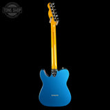 A blue electric guitar shown from the back against a solid black background, with a yellow neck and a Tone Shop watermark in the top-left corner.