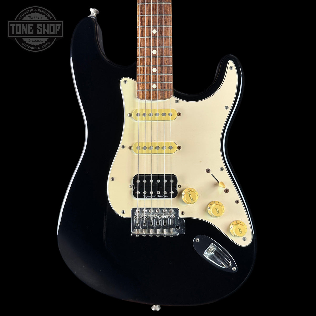 Black electric guitar with cream pickguard on a black background, featuring 'Tone Shop' logo.