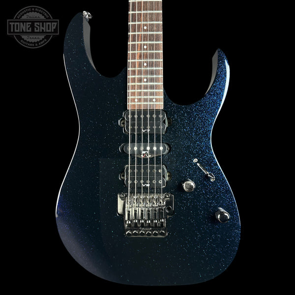 A close-up of an electric guitar body in a dark blue glitter finish, featuring a maple-shaped cutaway, dual humbucker pickups, chrome hardware, and a dark wood fretboard. A Tone Shop watermark is visible in the top-left corner.