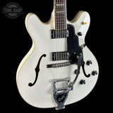 White electric guitar with a black pickguard on a black background, featuring the Tone Shop logo.