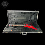 A red electric guitar inside an open black hard case with gray velvet lining, photographed against a black background. A Tone Shop watermark is visible in the top-left corner.