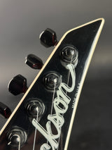 Close-up of a Gibson electric guitar headstock, showing the black glossy finish, six tuning pegs, white script Gibson branding, and 'MADE IN USA' text against a dark gray background.