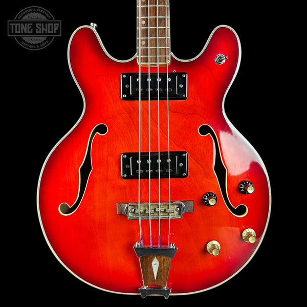 Red electric bass guitar with a black background, featuring the Tone Shop logo.