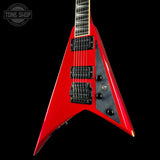 A red electric guitar with a distinctive angular body, black hardware, and a black pickguard, shown against a solid black background. A Tone Shop watermark is visible in the top-left corner.
