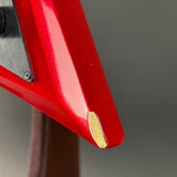 Close-up of a red electric guitar body corner with a gold-colored edge finish and a brushed metal control plate, shown against a neutral gray background.