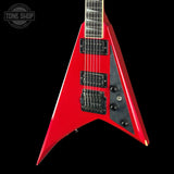 A red electric guitar with a distinctive angular body, black hardware, and a black pickguard, shown against a solid black background. A Tone Shop watermark is visible in the top-left corner.