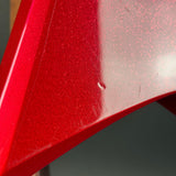 Close-up of a glossy red metallic surface with fine glitter/sparkle particles and a small white scratch or defect visible on the curved panel.