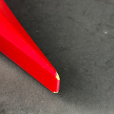 A close-up of a bright red, pointed object, possibly a stylus or a sharp tool tip, resting on a dark gray textured surface.