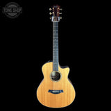 A Taylor acoustic-electric guitar with a natural wood finish and a cutaway body, shown against a solid black background with a Tone Shop watermark in the top-left corner.