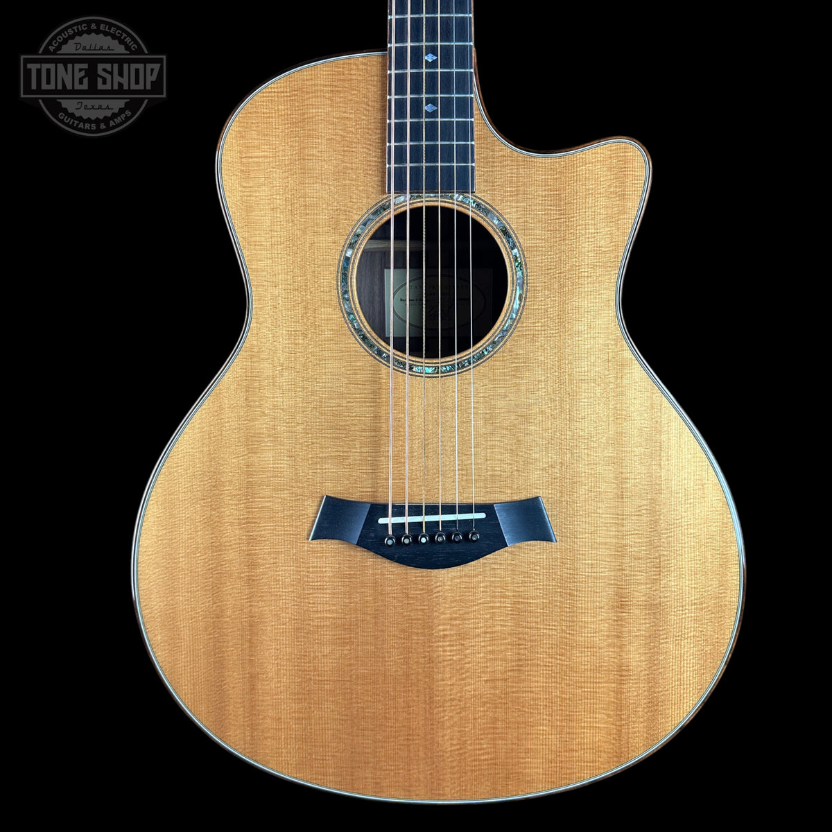 A front-facing acoustic guitar with a natural wood finish and a dark navy blue bridge, shown against a solid black background with a Tone Shop watermark in the top-left corner.