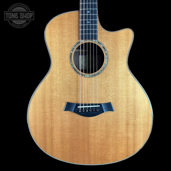 A front-facing acoustic guitar with a natural wood finish and a dark navy blue bridge, shown against a solid black background with a Tone Shop watermark in the top-left corner.
