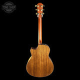 The back view of a wooden acoustic guitar with a cutaway body and six-string headstock, shown against a solid black background with a Tone Shop watermark in the top-left corner.