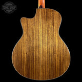 The back of an acoustic guitar with a rich, warm brown wood grain finish, shown against a solid black background with a Tone Shop watermark in the top left corner.